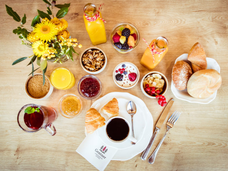 Große Auswahl an Frühstücksspeisen- & Getränken am Frühstücksbuffet vom 4 Sterne Hotel in Nürnberg, zusammen auf einem Holztisch mit Blumen angerichtet.